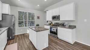 Una cocina moderna con armarios blancos, encimera de granito, refrigerador de acero inoxidable, microondas y horno.