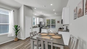 Una cocina moderna con armarios blancos, una mesa de comedor con sillas y una planta en maceta.
