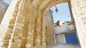 Un antiguo arco de piedra que da paso a una estrecha calle con una puerta azul y un farol.
