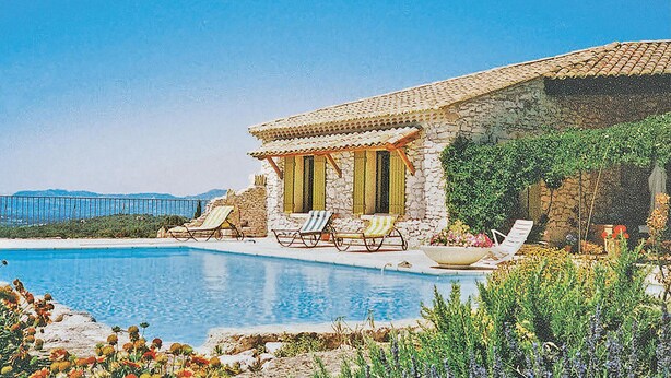 Una villa de piedra con piscina, dos tumbonas y vistas al mar.