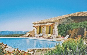 Une villa en pierre avec piscine, deux chaises longues et vue sur la mer.