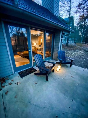 Uma casa com varanda coberta, duas cadeiras Adirondack e um tapete de boas-vindas.