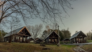 A row of rustic cabins with a grassy foreground and trees in the background. - Lazy Lake Days • Fast Wifi • Roku TV • Free Firewood (Alpine)