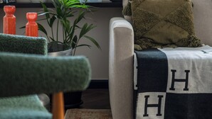 Una sala de estar con sofá, una silla verde, una planta en maceta y un ventanal con persianas.