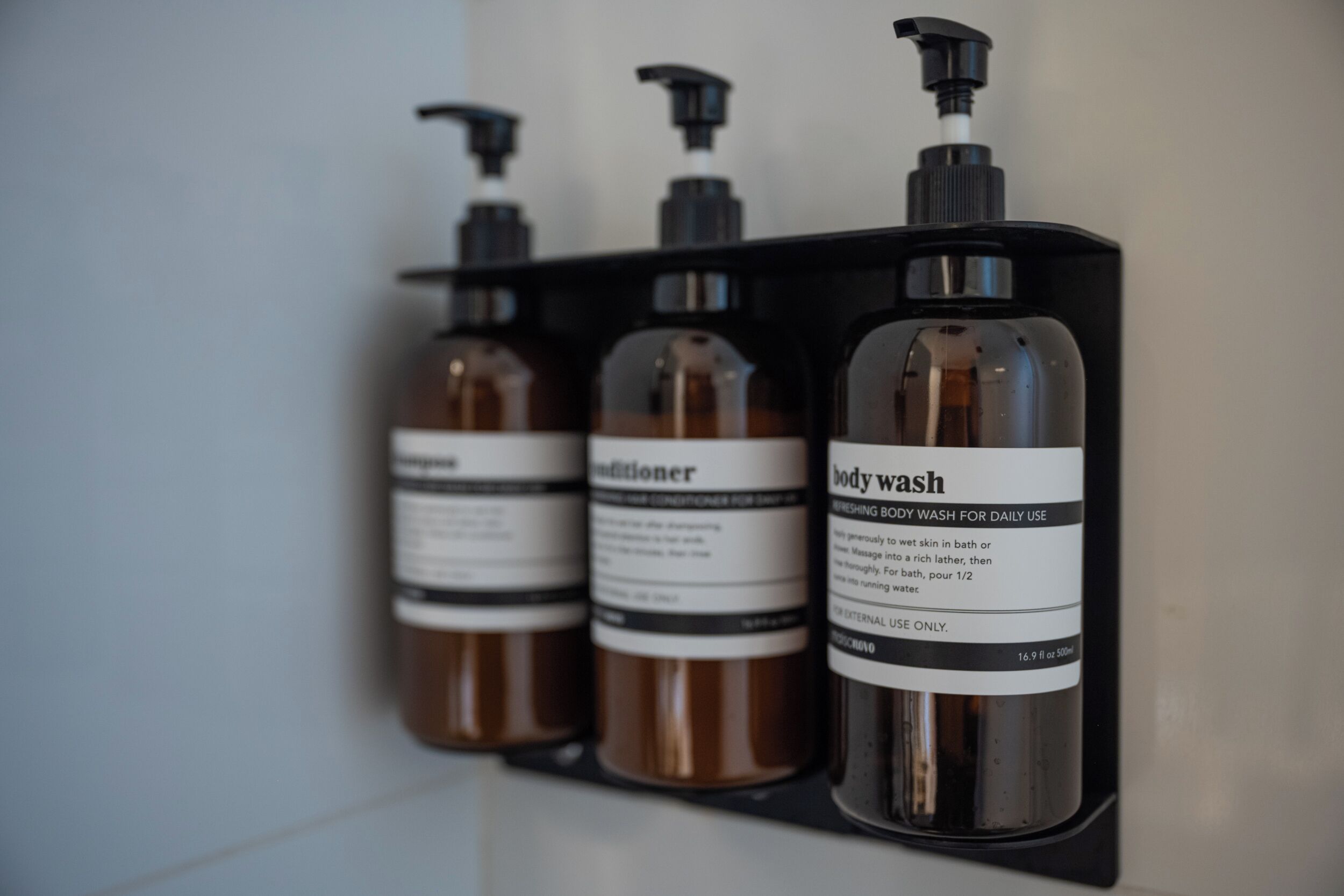 Trois bouteilles de gel douche et d’après-shampoing sur une étagère noire.