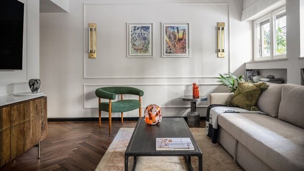 Una sala de estar moderna con un sofá, una mesa de centro, un sillón verde y dos obras de arte enmarcadas en la pared.