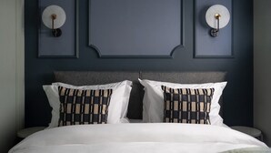 Una cama con sábanas blancas y dos almohadas estampadas con un diseño escocés, una pared azul oscuro y dos lámparas de pared.