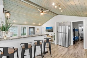 A modern kitchen with a central island, bar stools, a ceiling fan, and a refrigerator.
