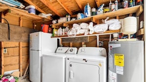 Un lavadero con ropa apilada, un refrigerador y varios productos de limpieza.
