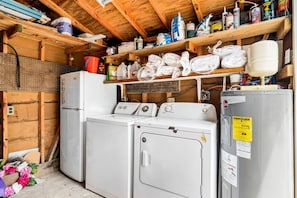 A laundry room with stacked laundry, a refrigerator, and various cleaning supplies.