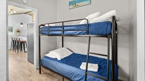 Una cama litera con ropa de cama azul, una almohada blanca y una toalla blanca en la cama inferior. Encima de la cama, hay un cuadro con una escena de playa.
