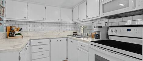 Een keuken met witte kastjes, een magnetron, een oven en een betegelde spatwand.