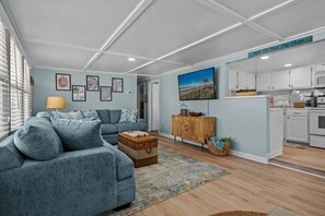 A modern living room with a sofa, a wooden cabinet, and a painting on the wall. - Ocean Lakes Cottage, Covered Patio, Grill and Beach! (Myrtle Beach)