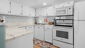 A kitchen with white cabinets, a microwave, an oven, and a coffee maker. - Ocean Lakes Cottage, Covered Patio, Grill and Beach! (Myrtle Beach)