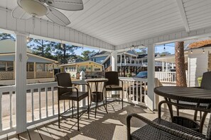 A covered outdoor seating area with wicker chairs and tables, overlooking a street with buildings. - Ocean Lakes Cottage, Covered Patio, Grill and Beach! (Myrtle Beach)