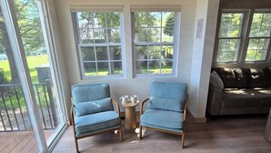 Ein Zimmer mit Holzboden, Holzbalkendecke, großen Fenstern, zwei blauen Stühlen, einem kleinen runden Tisch mit Tassen und einem braunen Sofa.