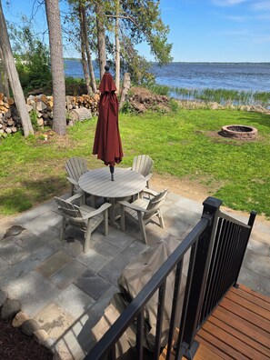 A patio with a round table and chairs, a covered umbrella, and a fire pit. - The Lily Pad: Newly Renovated, Lakefront Retreat on Shawano Lake, Sleeps 6 (Shawano)
