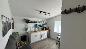 Een kleine keuken met witte kastjes, een houten aanrechtblad, en een eethoek met een tafel en stoelen.