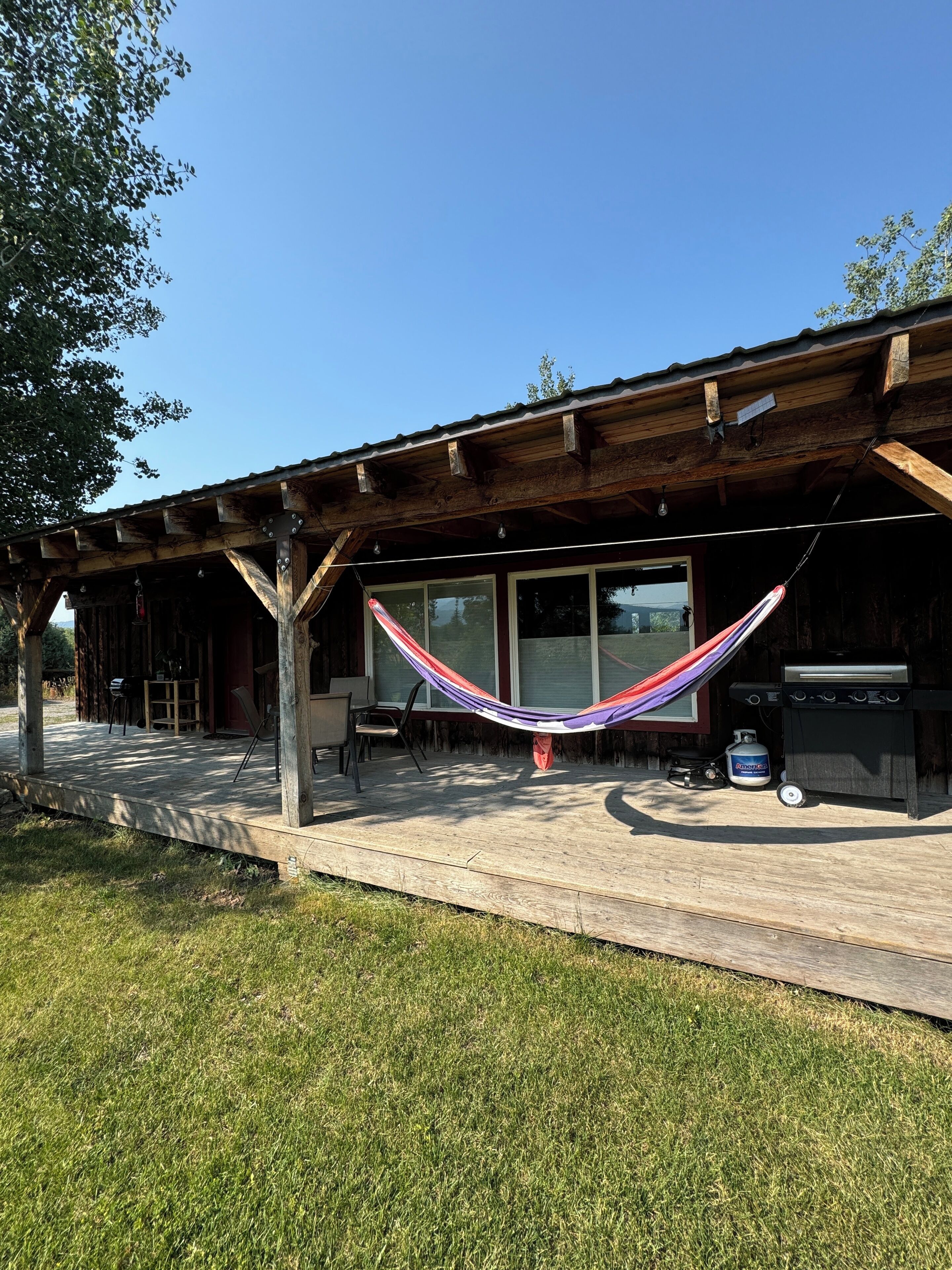 A wooden structure with a covered patio, a hammock, and a barbecue grill.