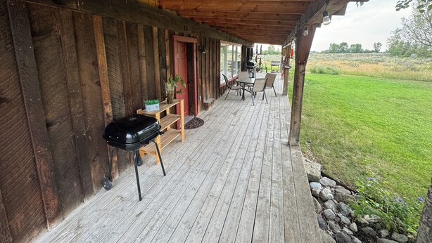 Een houten terras met een barbecue, zitplaatsen buiten en uitzicht op het omliggende landschap.