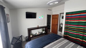 Een slaapkamer met een bed, een televisie, een houten deur en een kleurrijk gestreept gordijn.