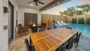 Eine Terrasse im Freien mit Holztisch und -stühlen, einem Deckenventilator und einem Pool.