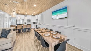 Eine moderne Küche mit weißen Schränken, einem Holzespeisetisch, gedeckt für vier Personen, und einem großen Fenster mit Blick auf einen Strand.