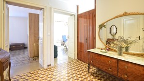 Ein Flur mit gemusterten Bodenfliesen, ein Holzschrank mit Spiegel und eine Kommode mit einer Vase getrockneter Blumen.