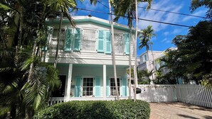 A two-story house with a white exterior and turquoise shutters, surrounded by lush greenery and a white picket fence. - Seaport Serenity Cottage - Quiet and Quaint (Key West)