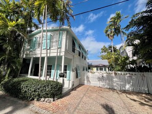 A two-story house with a white exterior and green shutters, surrounded by a white picket fence and palm trees. - Seaport Serenity Cottage - Quiet and Quaint (Key West)