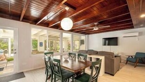 A spacious room with a wooden ceiling, a dining table with chairs, a sofa, and a TV mounted on the wall. - Plumeria Paradise, Your Tropical Retreat Close to the Beach (Key West)
