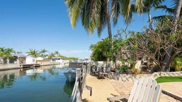 A waterfront area with a boat dock, a chair, and palm trees. - Private & Haven-ly - Pool Home on Boating Canal (Key Haven)