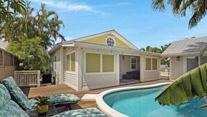 A single-story house with a pool, surrounded by palm trees and a wooden deck.