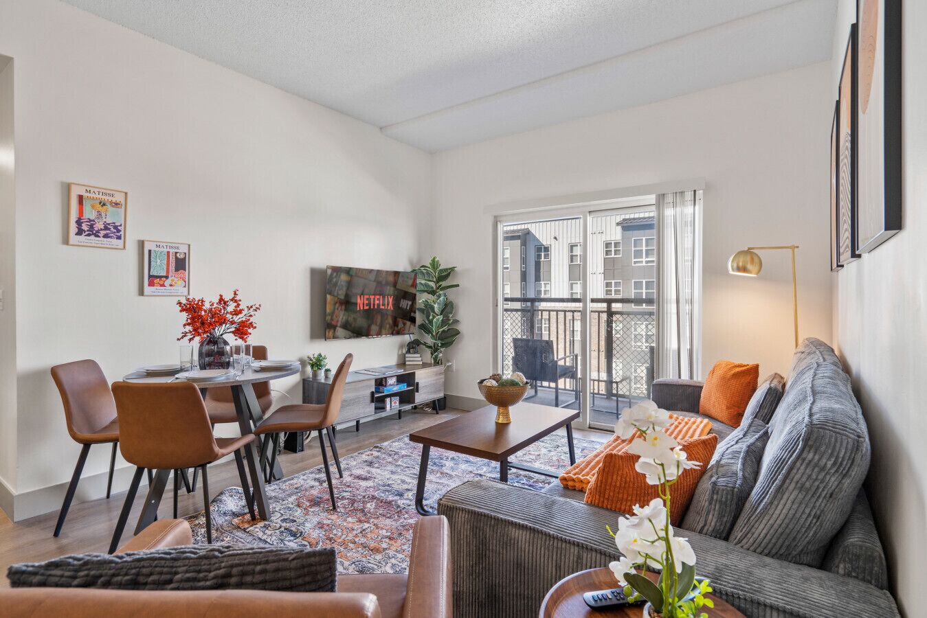 A modern living room with a dining area, a sofa set, a coffee table, and a TV mounted on the wall.