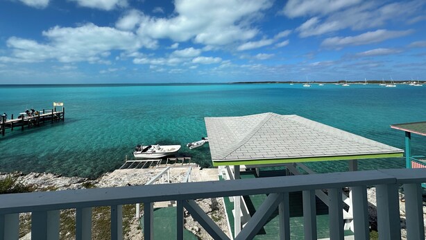 A clear view of turquoise waters, a dock with boats, and a covered area with a tiled roof. - Charming 1-bedroom apartment in beautiful Black Point with amazing views (Black Point)