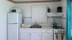 A compact kitchen with white cabinets, a microwave, a sink, a stove, and a window with blinds. - Charming 1-bedroom apartment in beautiful Black Point with amazing views (Black Point)