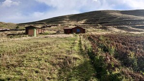 A rural landscape with two small buildings, one with a green door and another with a blue window, surrounded by grassy fields and rolling hills under a partly cloudy sky. - Charming Rural House in Yanaoca (Yanaoca)