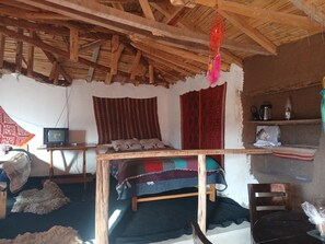A rustic room with a wooden ceiling, a bed with a colorful blanket, a television, and a shelf with a kettle and a plastic bottle. - Charming Rural House in Yanaoca (Yanaoca)