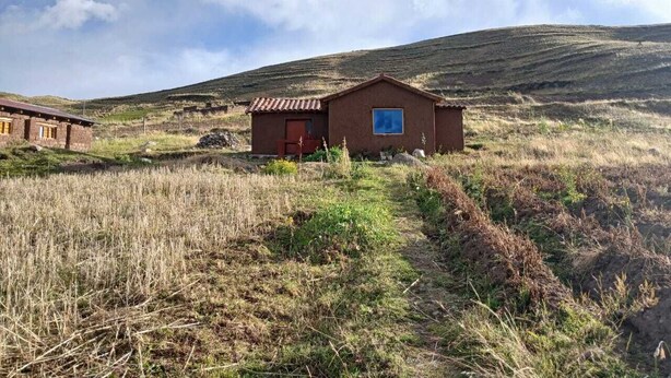 A rustic cabin with a red door and a blue window, surrounded by grassy terrain and hills. - Charming Rural House in Yanaoca (Yanaoca)