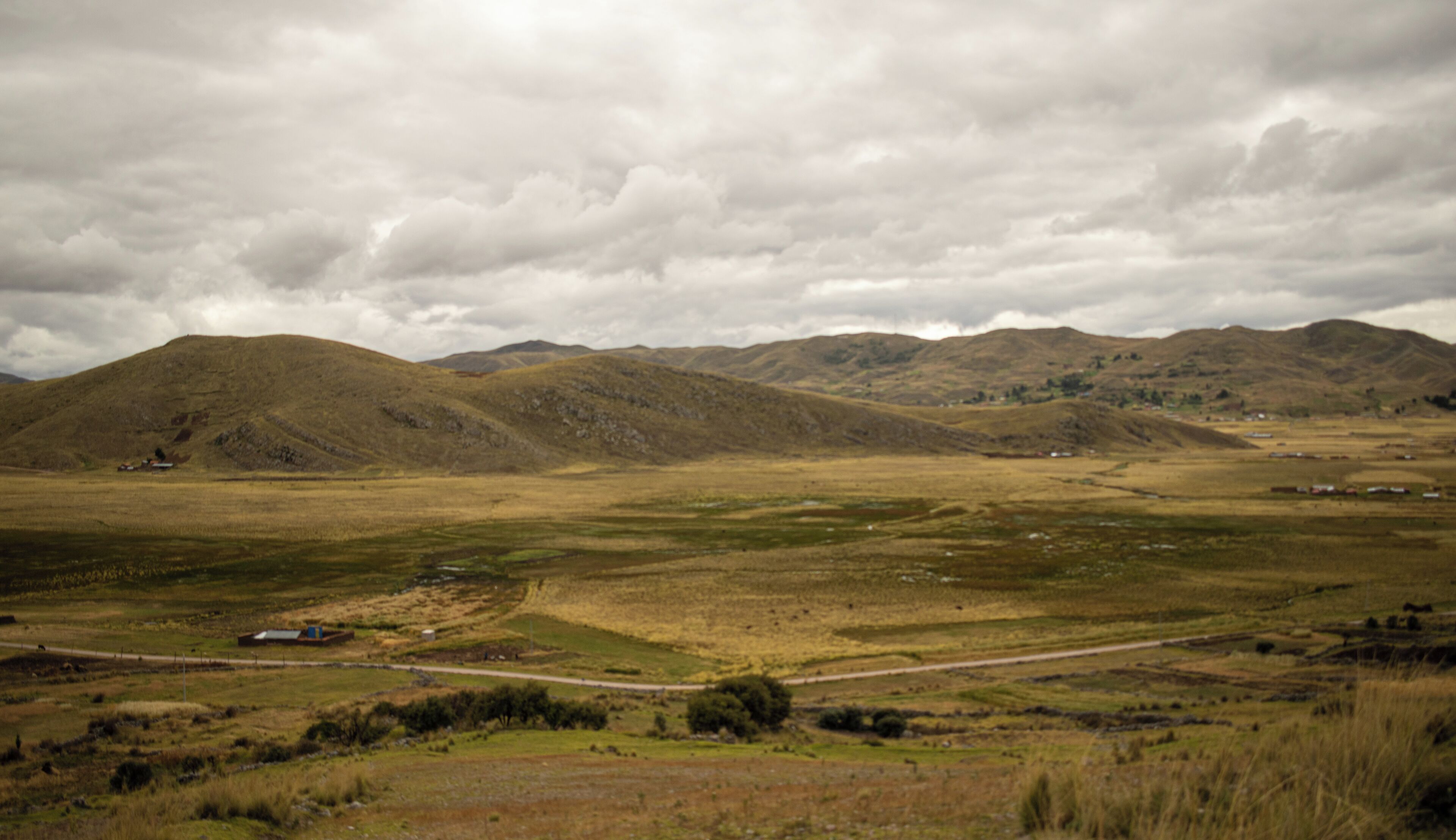 A rural landscape with rolling hills, a dirt road, and scattered buildings.