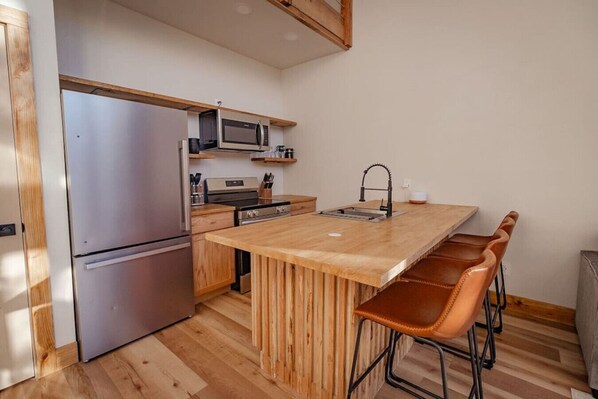 A compact kitchen with a central island, stainless steel appliances, and wooden bar stools.
