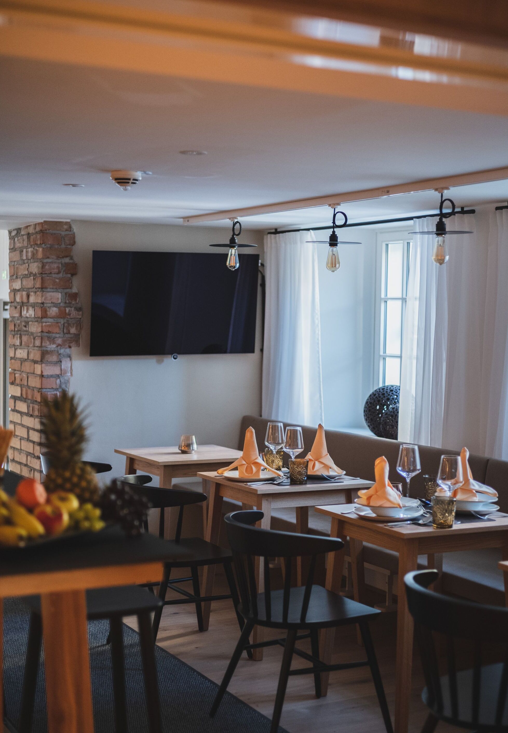 A dining area with wooden tables and chairs, a TV mounted on the wall, and a brick wall.