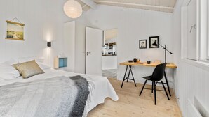 Un dormitorio con una cama, mesita de noche y un escritorio con una silla. Hay una ventana y una puerta que da al baño.