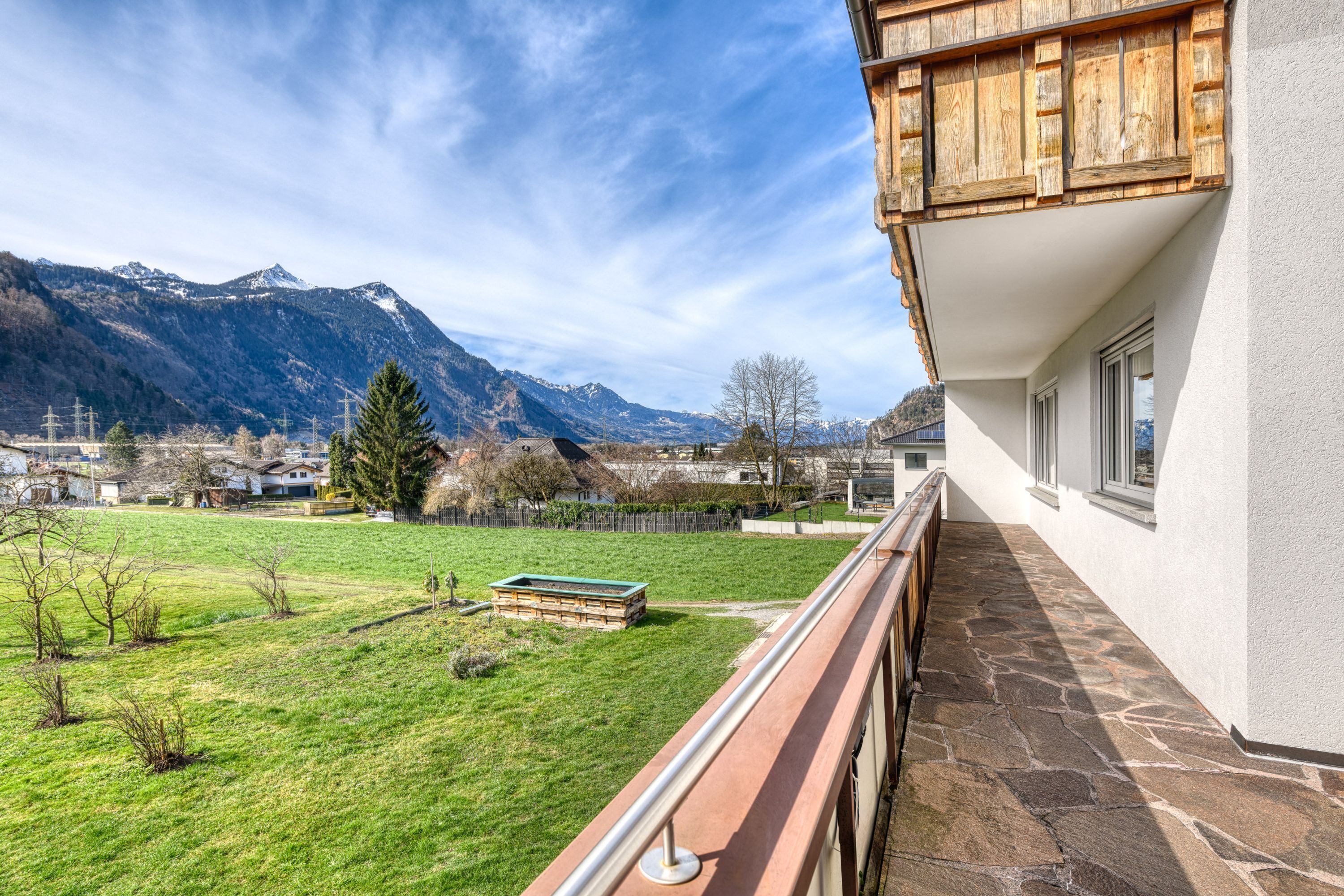 Ein Balkon mit Steinboden, Blick auf ein grünes Feld und Berge im Hintergrund.