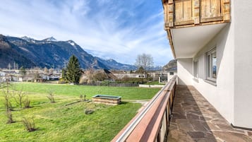 Ein Balkon mit Steinboden, Blick auf ein grünes Feld und Berge im Hintergrund.