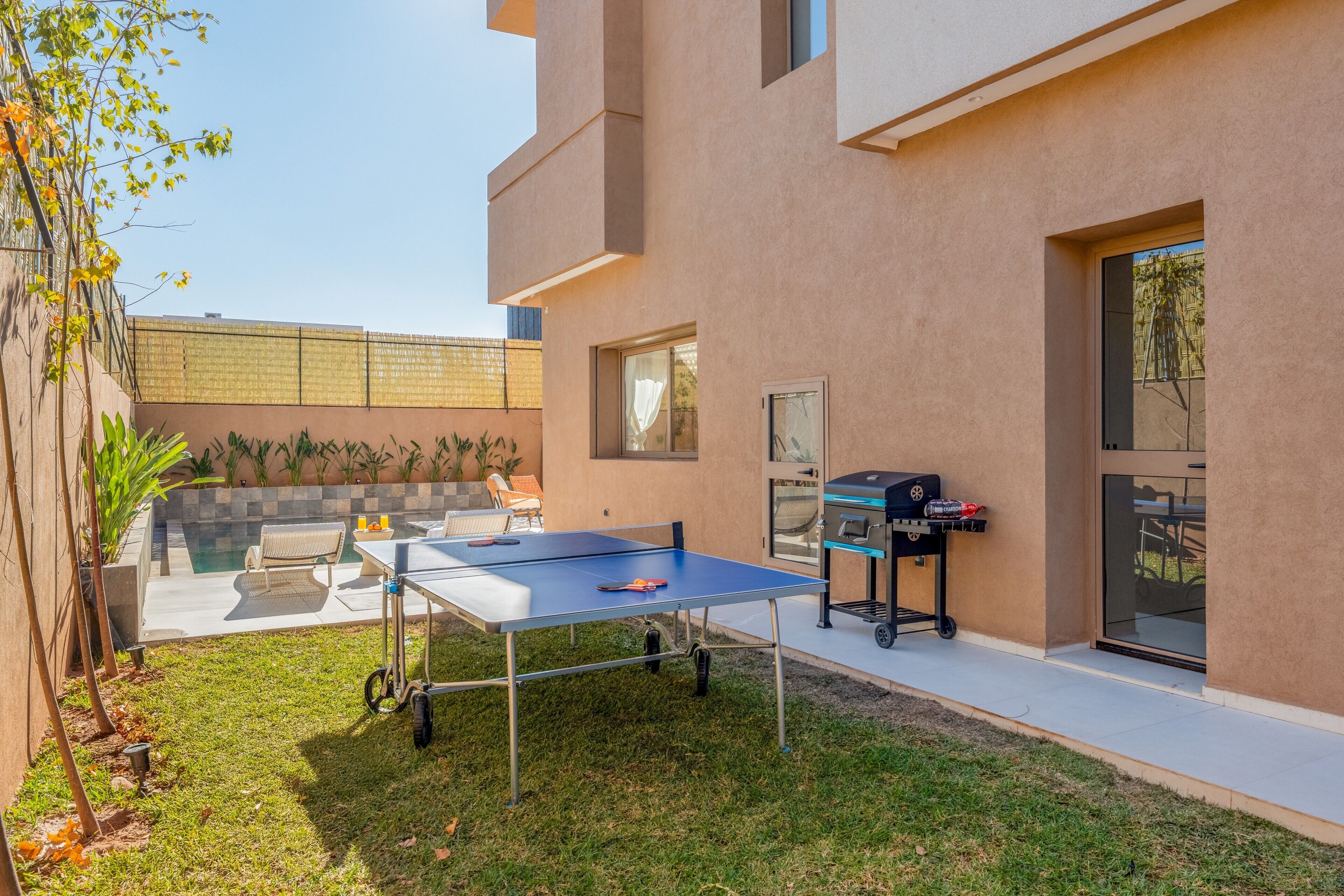 A modern outdoor patio with a ping pong table, a barbecue grill, and a seating area.