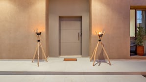 A modern building entrance with a neutral-colored door, two wooden tripods with lights, and a potted plant to the right. - Villa Yas - 5-Stars - Heated Pool - Driver - Chef - Games - 15min to City Center (Marrakech)