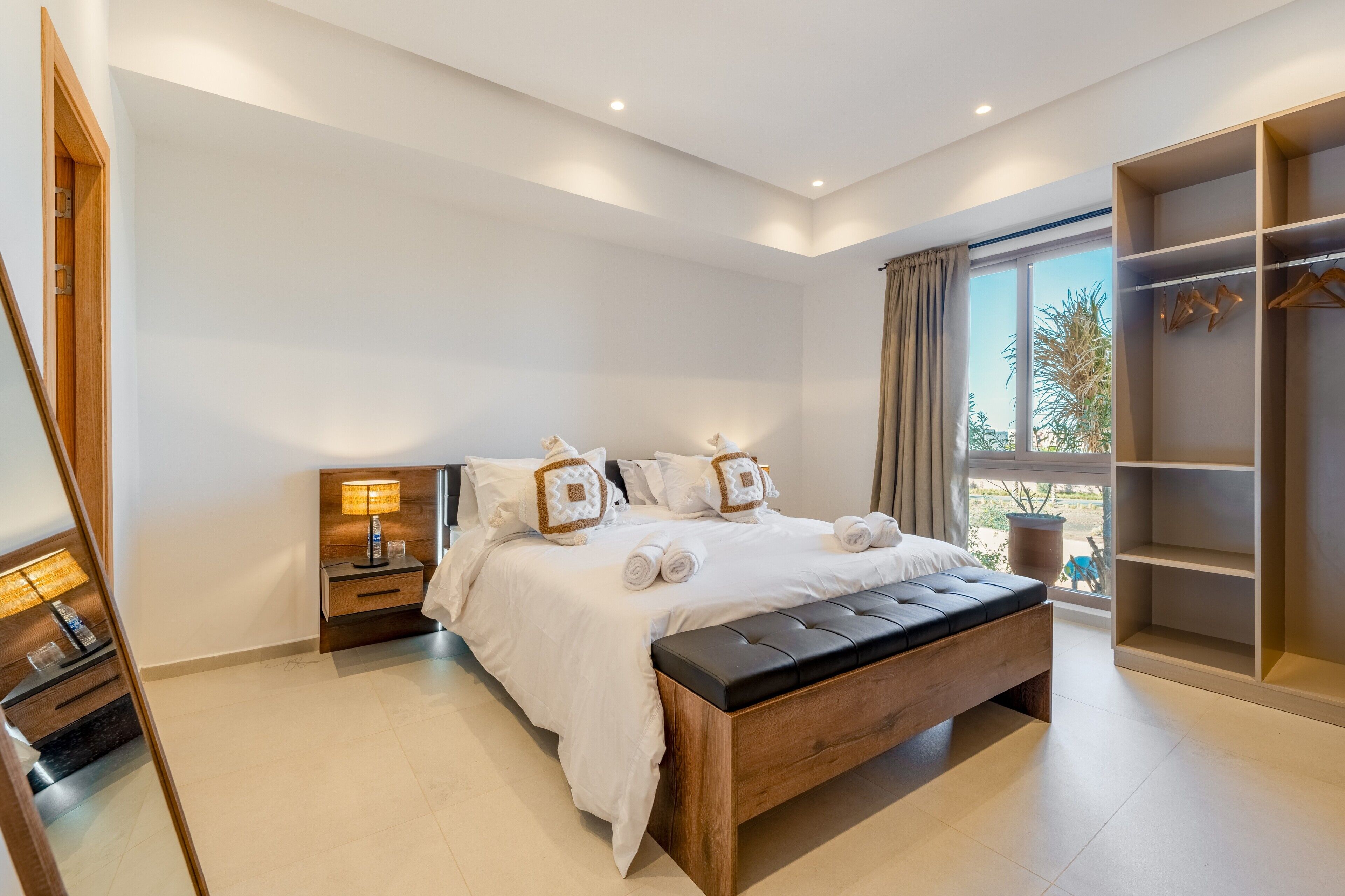 A modern bedroom with a large bed, bedside tables, a wardrobe, and a view of the outdoors.