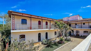 A two-story building with balconies, a garden area, and a clear blue sky. - Refúgio Tiradentes (Tiradentes)