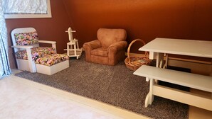 Una habitación acogedora con una pared marrón, una pequeña mesa blanca, un sillón con cojín, una pequeña mesa blanca con un cojín estampado y una cesta de mimbre.